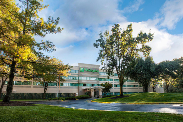 Hotel building with green signage surrounded by lush trees under a blue, partly cloudy sky.