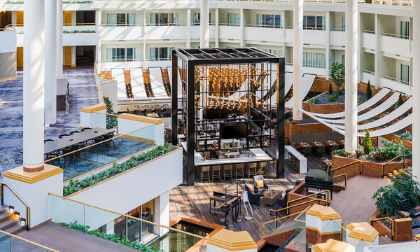 Modern hotel courtyard with outdoor seating, central fire pit structure, and terraced landscaping.