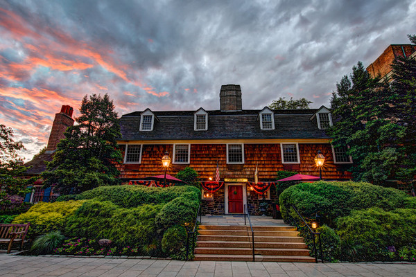 Historic wooden building under dramatic sunset sky with lush green landscaping.