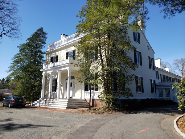 White historic mansion with columns and trees on a sunny day.