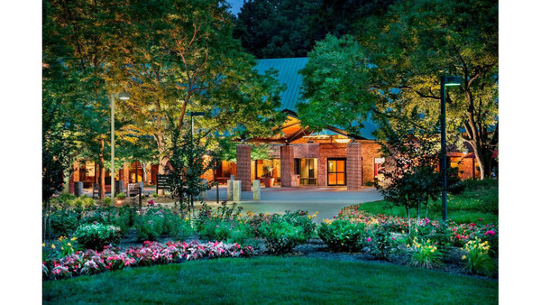 Modern brick building nestled among lush trees and manicured garden at dusk.