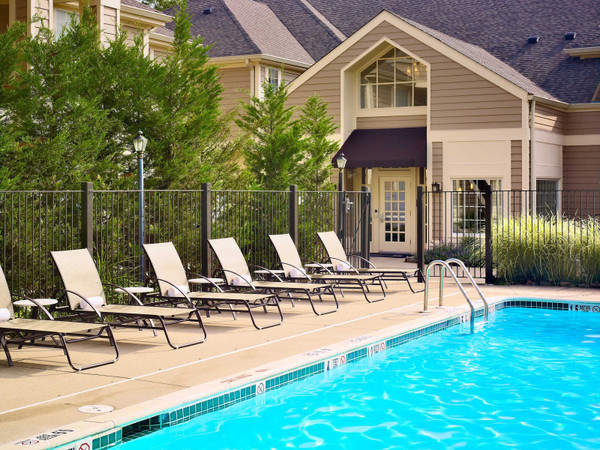 Poolside loungers in front of a modern, upscale residential building with lush greenery.