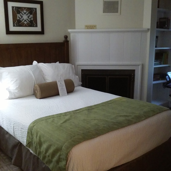 Bedroom with large white bed, brown headboard, and fireplace mantel.