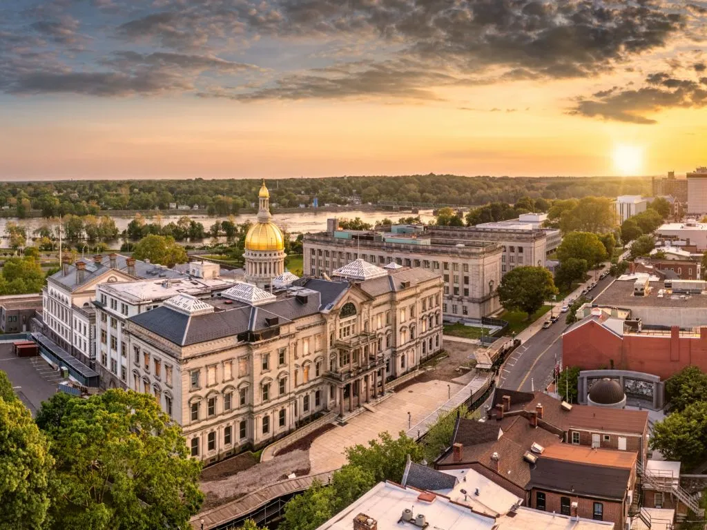 Historic European-style building overlooking a river and city skyline at sunset.