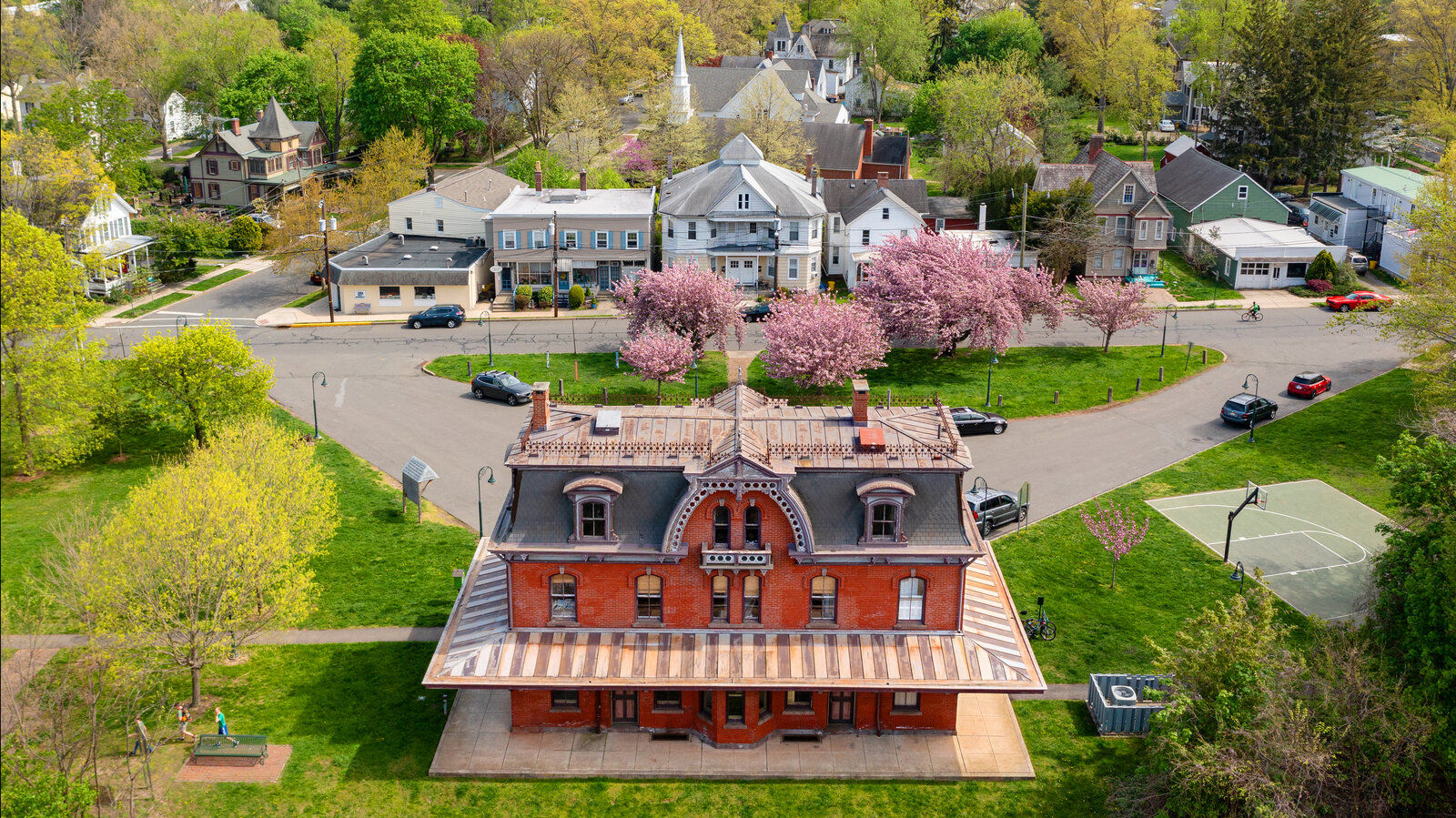 Victorian house in a leafy, suburban neighborhood with blooming pink trees.