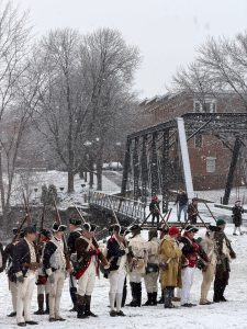 Revolutionary War reenactors in period uniforms stand in formation during snowfall in Trenton.